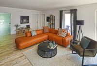Wohnzimmer mit einer orangen Couchgarnitur im Musterhaus des Immobilienmaklerb&uuml;ros Poort &amp; Koch Projektbau aus Elmshorn